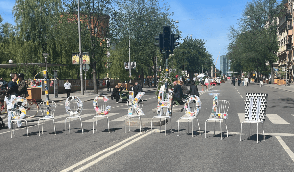 A row of chairs in the middle of the road have large, multicolored letters on them spelling out 'Stockholm'